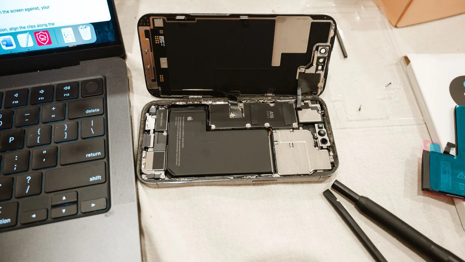 Вскрытый iPhone на столе мастера: видно аккумулятор и плату, рядом лежит новая батарея